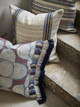 Azteque indoor printed cushion in coral, with pop art and ombre fringe trims in front of japura cushion with railroad trim